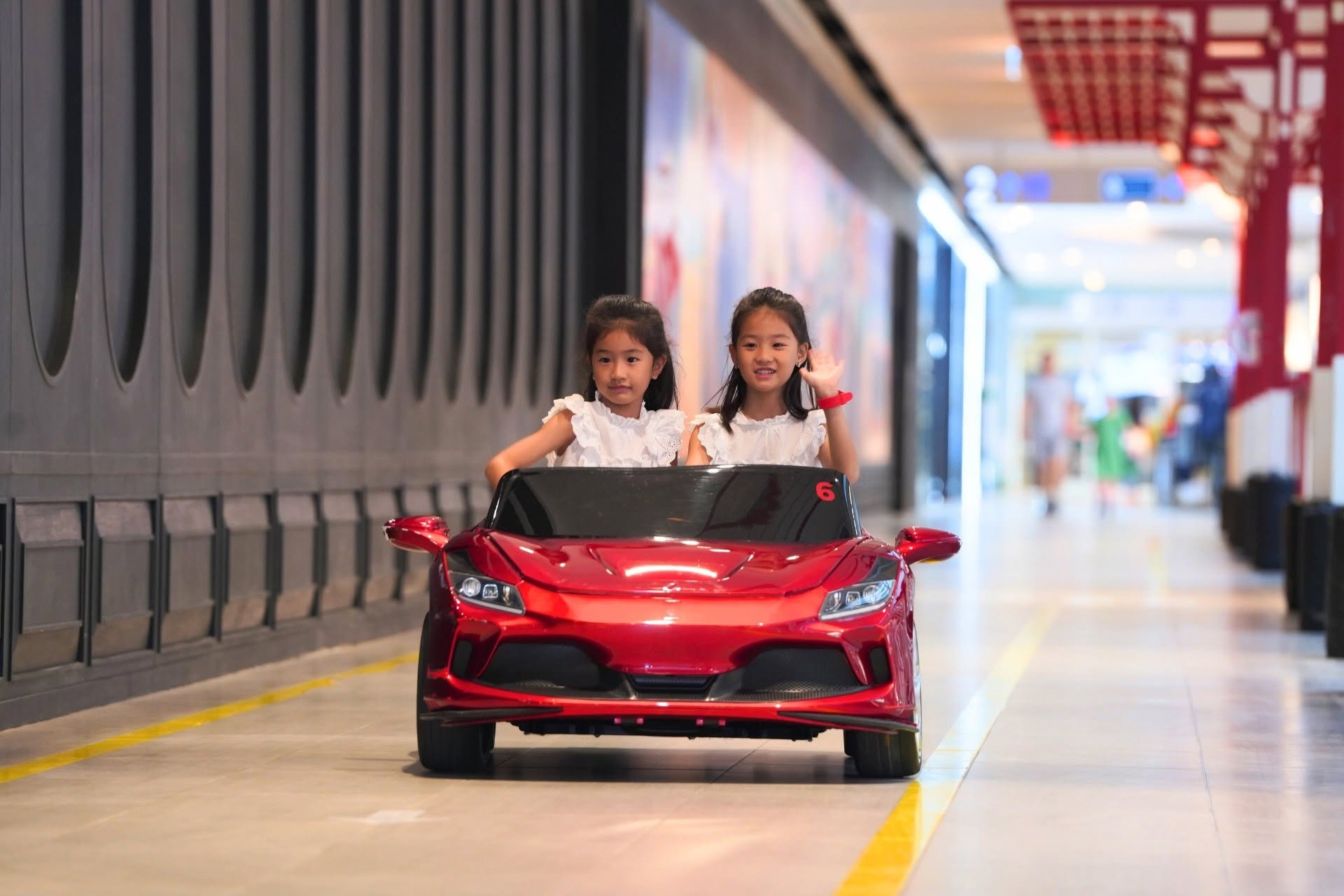 two children in red toy car indoors