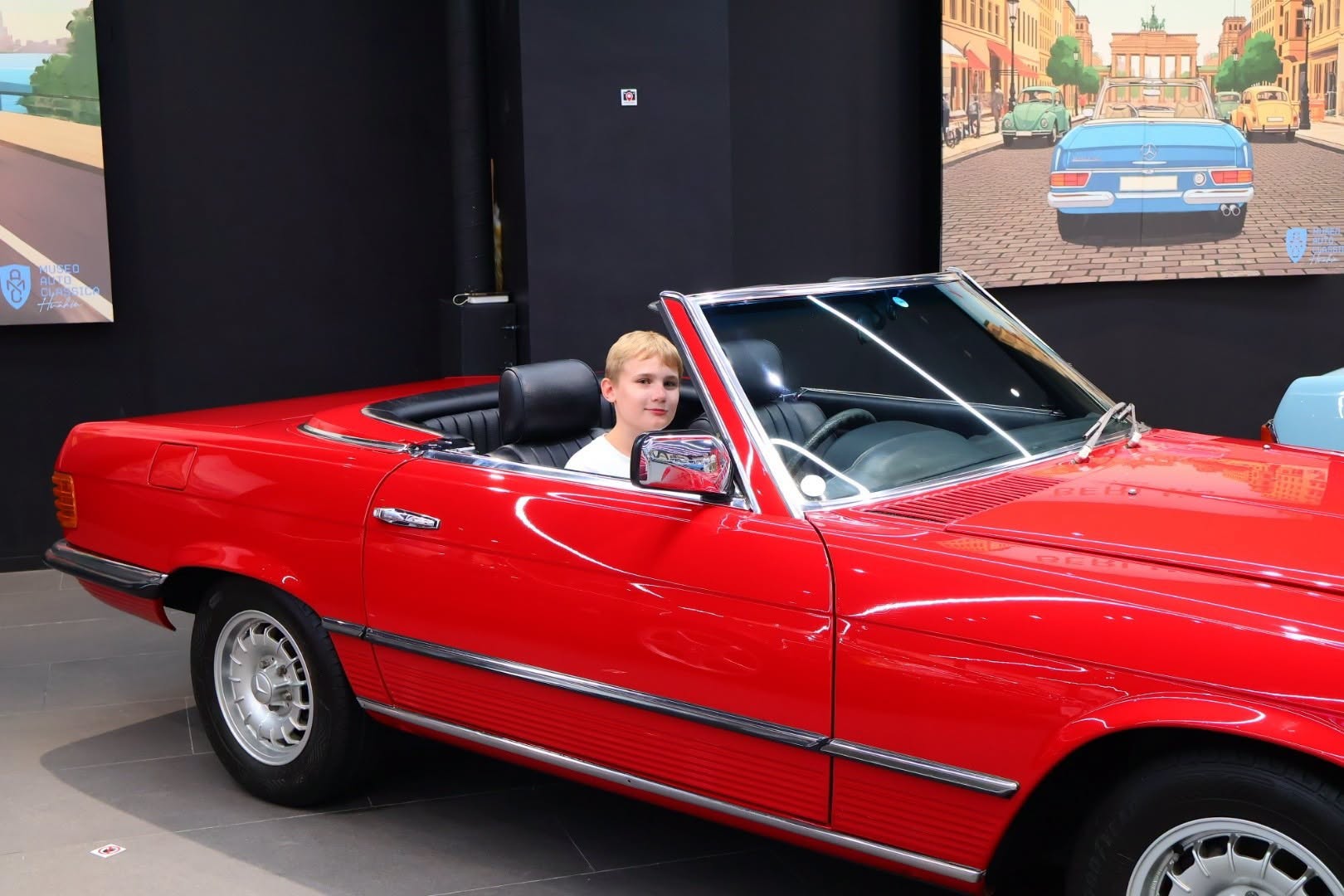 child sitting in red convertible with screens